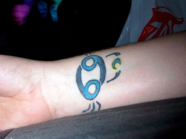 The Cancer Zodiac Tattoo on the wrist with blue ink design makes a make to look classy