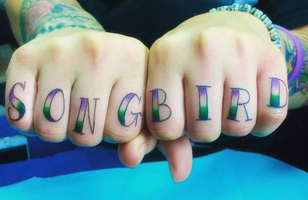 Knuckle Tattoo with the purple and green ink design make a man have an eye-catching look