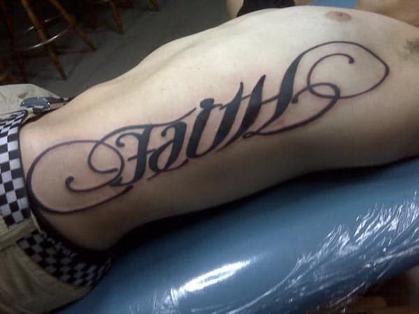 black bold Faith tattoo on side of abdomen and chest