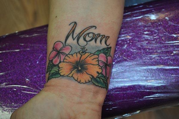Mom tattoo on the wrist with an orange flower design makes a girl appear charming 