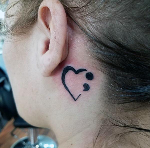 Semicolon tattoo on the back of the ear with a brown ink design brings the captivating look