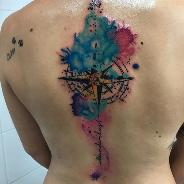 Charming compass with cardinal direction watercolor splashed tattoo ideas on back for adventure seeking women