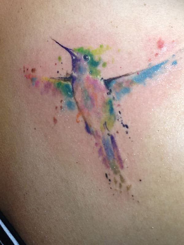 Flying humming bird watercolor tattoo on back for free-spirited women