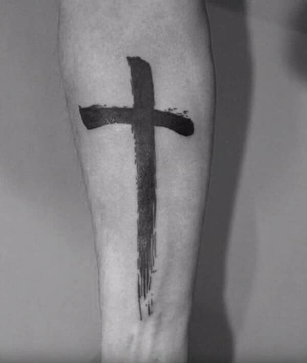 A striking paint stroke black cross tattoo design on forearm for Guys
